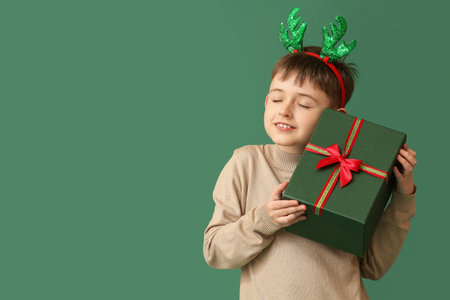 Funny little boy with reindeer horns and Christmas gift on color backgroundの写真素材