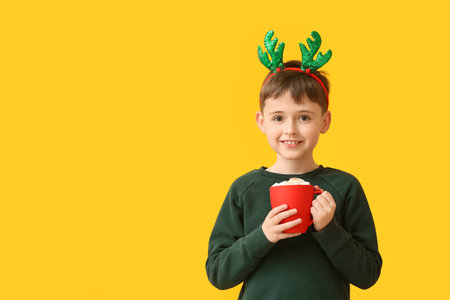 Funny little boy with reindeer horns and hot chocolate on color backgroundの写真素材