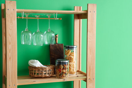 Wooden shelving unit with food, board and glasses near green wall