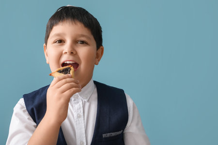 Little Jewish boy with tasty Hamantaschen for Purim holiday on gray backgroundの写真素材
