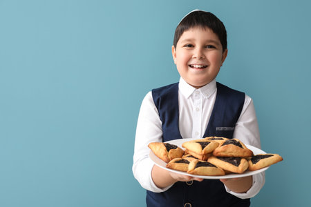 Little Jewish boy with tasty Hamantaschen for Purim holiday on gray backgroundの写真素材