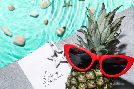 Pineapple with sunglasses and greeting card for Merry Christmas near swimming poolの写真素材
