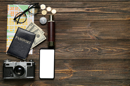 Guide's belongings with mobile phone and city map on dark wooden background