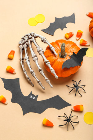 Paper bats with Halloween pumpkin, skeleton hand and candy corns on beige backgroundの写真素材