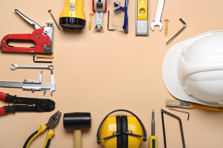Frame made of builder's tools with hearing protectors on beige background