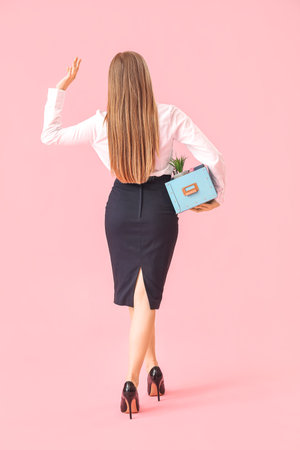 Fired young woman with packed personal stuff waving hand on pink background, back viewの写真素材