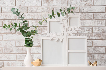 Family tree with photo frames, eucalyptus branches in vase and decor on table near brick wall