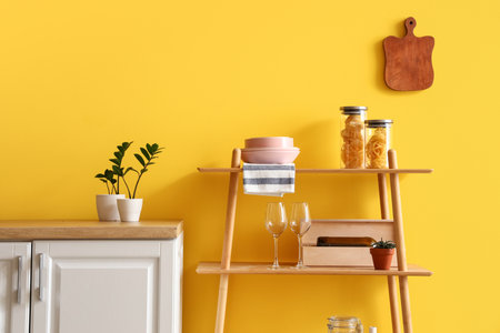 Modern shelving unit with dishware and houseplants near yellow wall in kitchenの写真素材