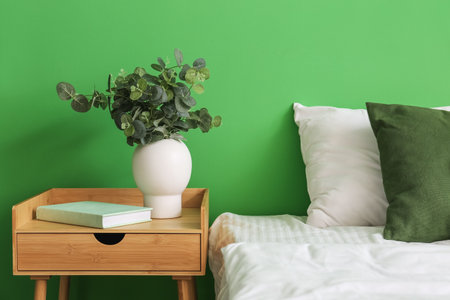 Bedside table with book and eucalyptus in vase near green wallの写真素材