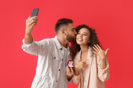 Engaged young couple taking selfie on color backgroundの写真素材