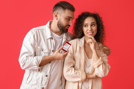 Young man proposing to his girlfriend on color background