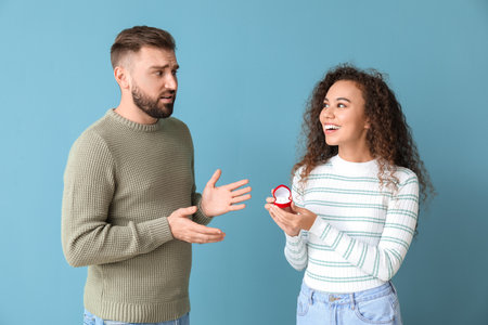 Young woman proposing to her confused boyfriend on color background
