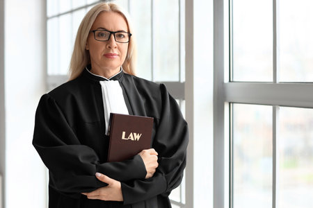 Mature female judge with law book near window in courtroomの写真素材
