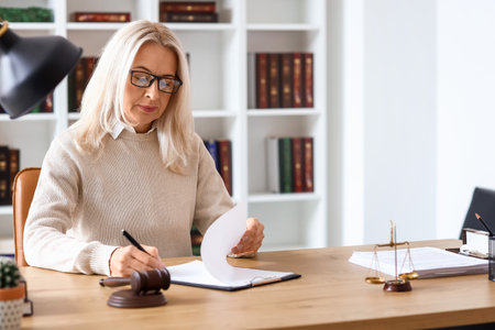 Mature female judge working with document at table in courtroomの写真素材