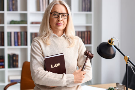 Mature female judge with gavel and law book in courtroomの写真素材