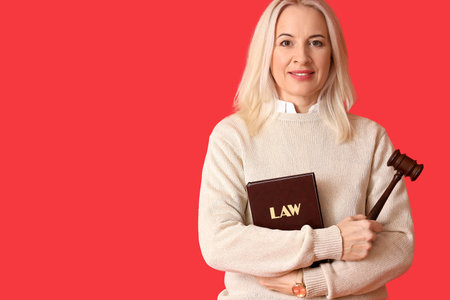Mature female judge with gavel and law book on red background
