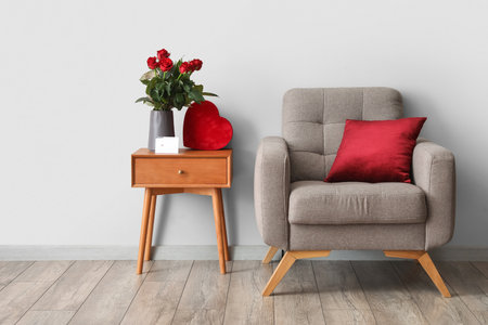 Bouquet of flowers and gift for Valentine's Day on table near armchair in interior of roomの写真素材