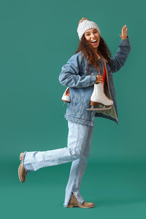 Beautiful young woman in winter clothes and with ice skates on color background