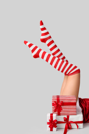 Sexy young woman in Christmas stockings and with gift boxes on light backgroundの写真素材