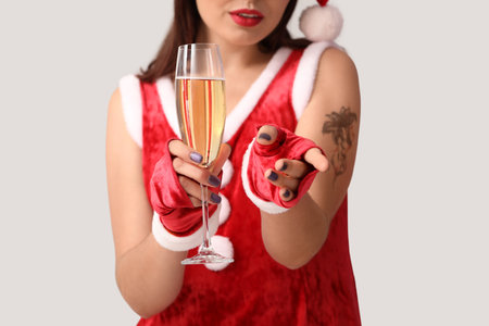 Sexy young woman in Santa costume and with champagne on light backgroundの写真素材