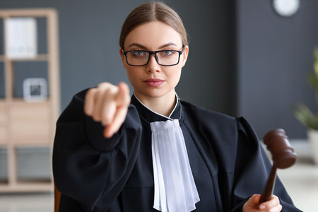 Young female judge with gavel pointing at viewer in courtroomの写真素材