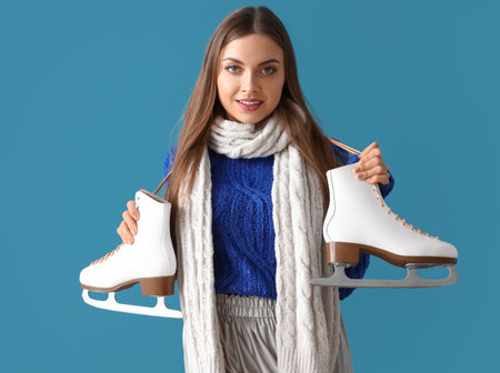 Beautiful young woman in winter clothes and with ice skates on color backgroundの写真素材