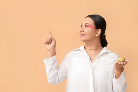 Beautiful Asian woman with tasty Japanese mochi pointing at something on color backgroundの写真素材