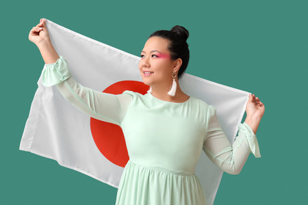 Beautiful young Asian woman with flag of Japan on green backgroundの写真素材