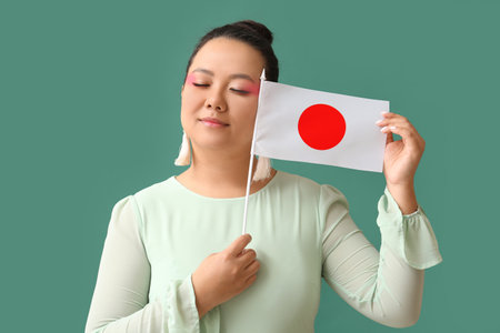 Beautiful young Asian woman with flag of Japan on green backgroundの写真素材