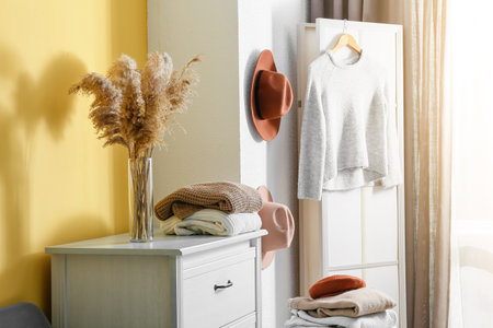 Warm sweaters and vase on chest of drawers near yellow wall in room