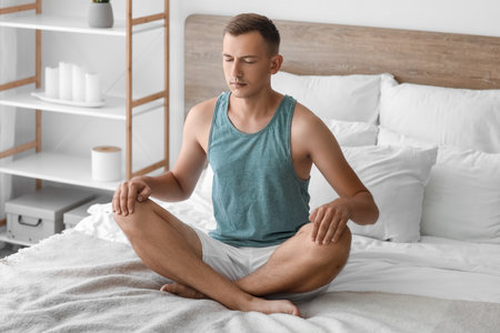 Young man meditating on bed at homeの写真素材