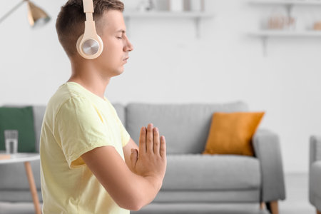 Young man with headphones meditating at homeの写真素材