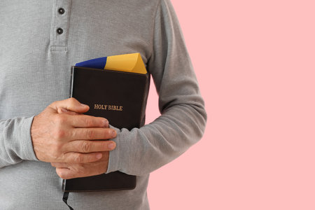 Mature man with Holy Bible and flag of Ukraine praying on pink background, closeupの写真素材