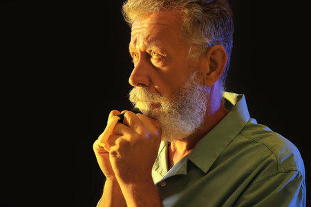 Mature man with lights in colors of Ukrainian flag praying on black background, closeup