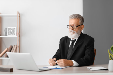 Male psychologist with laptop video chatting at table in officeの写真素材