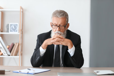 Mature businessman praying at table in officeの写真素材