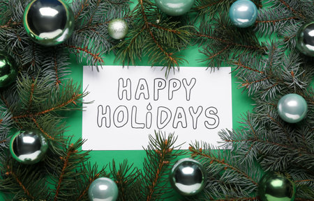 Greeting card with text HAPPY HOLIDAYS, fir tree branches and Christmas balls on green background