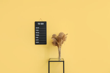 To-do list and vase with pampas grass on table near yellow wallの写真素材