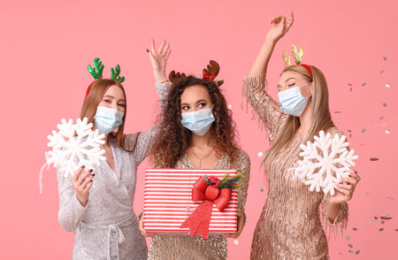 Beautiful young women in medical masks and with Christmas gift on color backgroundの写真素材