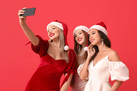Beautiful young women in Santa hats taking selfie on color backgroundの写真素材