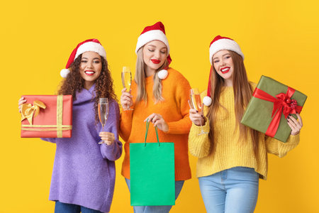 Beautiful young women with Christmas gifts and glasses of champagne on color backgroundの写真素材