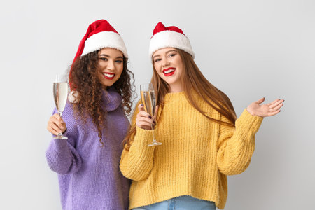 Beautiful young women in Santa hats and glasses of champagne on light backgroundの写真素材