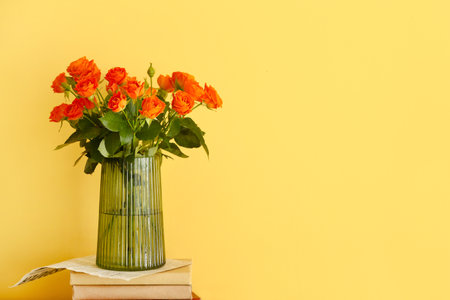 Vase with bouquet of beautiful roses with books on yellow backgroundの写真素材