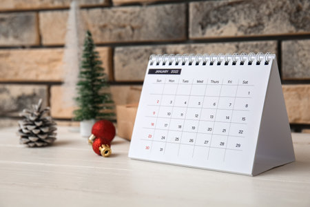 Paper calendar for January 2022 and Christmas decor on white wooden table near brick wallの写真素材