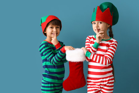 Cute little children in elves costumes and with Christmas sock on color backgroundの写真素材