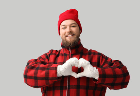 Young man making heart shape with his hands in warm gloves on light backgroundの写真素材