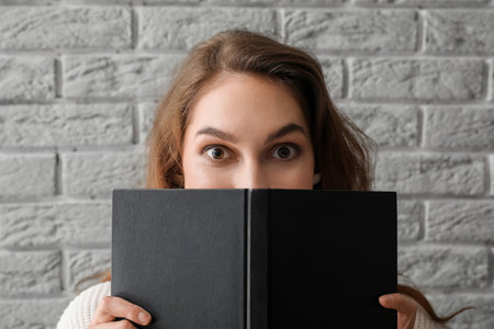 Young woman holding opened book near gray brick wallの写真素材