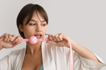 Beautiful young woman with mouth gag on gray backgroundの写真素材