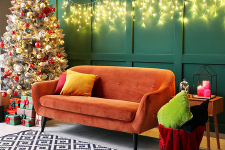 Red sofa with Christmas tree, gifts and glowing lights near green wallの写真素材