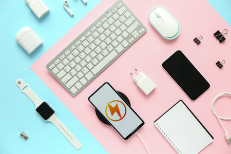 Different modern gadgets and mobile phone charging with wireless pad on color background